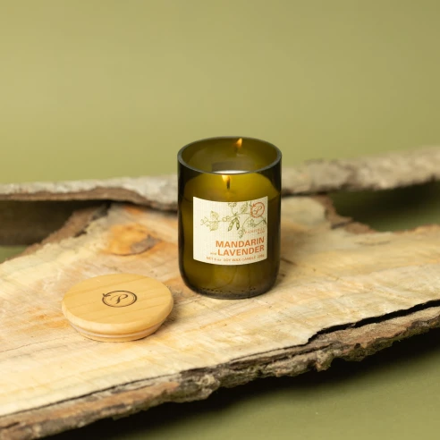 Vela Paddywax Eco Mandarin & Lavender encendida sobre corteza de madera, con su tapa de madera grabada al lado