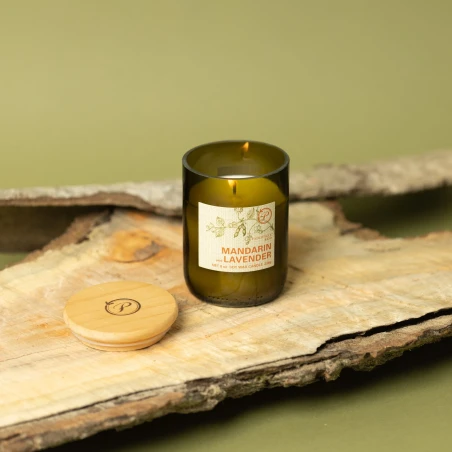 Vela Paddywax Eco Mandarin & Lavender encendida sobre corteza de madera, con su tapa de madera grabada al lado