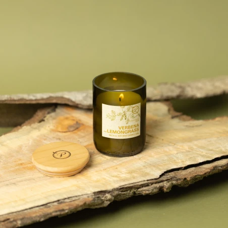 Vela Paddywax Eco Verbena & Lemongrass encendida sobre corteza de madera, con su tapa de madera grabada al lado
