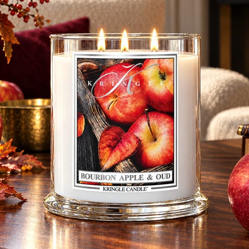 Vela Kringle Candle Bourbon Apple & Oud de 3 mechas encendida en un salón otoñal con chimenea y manzanas rojas