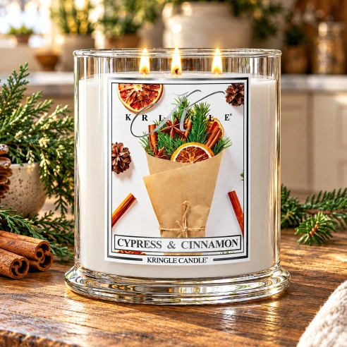Vela Kringle Candle Cypress & Cinnamon de 3 mechas encendida en una cocina con ramas de abeto, piñas y canela