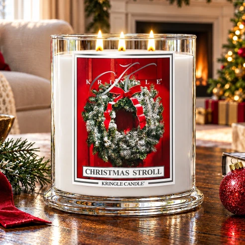Vela Kringle Candle Christmas Stroll de 3 mechas encendida en un salón navideño con chimenea, guirnaldas y árbol de Navidad