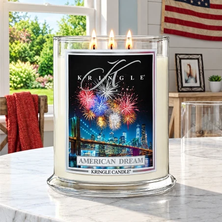 Vela Kringle Candle American Dream de 3 mechas encendida en una mesa de mármol con la bandera de EE. UU. al fondo