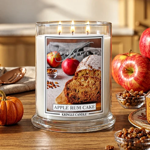 Vela Kringle Candle Apple Rum Cake de 3 mechas encendida en una mesa de cocina con manzanas, calabazas y pasas