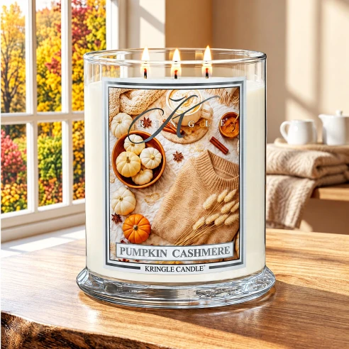 Vela Kringle Candle Pumpkin Cashmere de 3 mechas encendida en una mesa de madera junto a una ventana con árboles otoñales