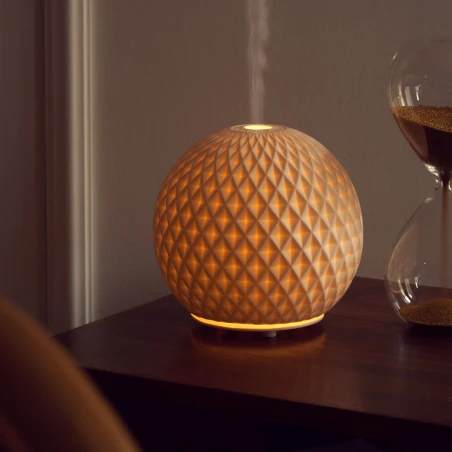 Difusor eléctrico Maison Berger Sphère encendido en un salón, junto a un reloj de arena