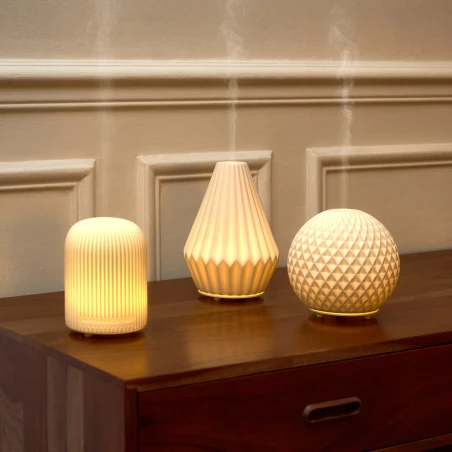 Difusores eléctricos Maison Berger Dôme, Cône y Sphère encendidos sobre una cómoda de madera