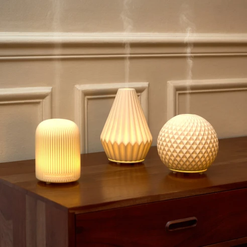 Difusores eléctricos Maison Berger Dôme, Cône y Sphère encendidos sobre una cómoda de madera