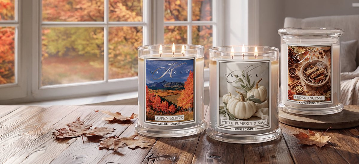 Velas grandes de tres mechas de Kringle Candle encendidas junto a una ventana en otoño